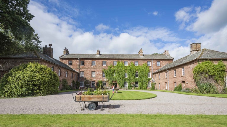 View of the front of the house with a garden trolley and children playing domino at Acorn Bank, Cumbria